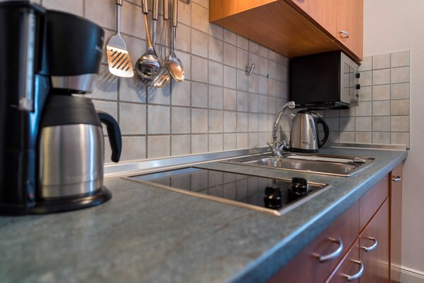 Une cuisine équipée d’une machine à café, d’une bouilloire et d  ’ustensiles de cuisine, le tout posé sur le plan de travail.