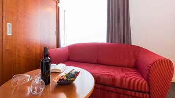 Una habitación con un sofá rojo, una mesa de madera con una botella de vino, copas y un cuenco de aperitivos.
