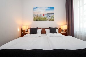 A hotel room with a large bed, two bedside lamps, a wall-mounted painting, and a window with curtains.