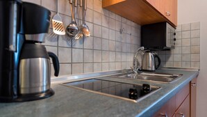 Une cuisine équipée d’une machine à café, d’une bouilloire et d’ustensiles de cuisine, le tout posé sur le plan de travail.