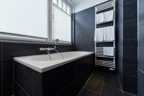 Une salle de bain moderne avec une baignoire, un porte-serviettes et des carreaux de couleur foncée.