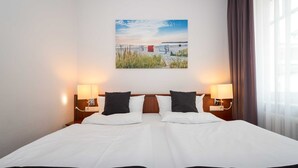 Une chambre d’hôtel avec un grand lit, deux lampes de chevet, un tableau accroché au mur et une fen être avec des rideaux.