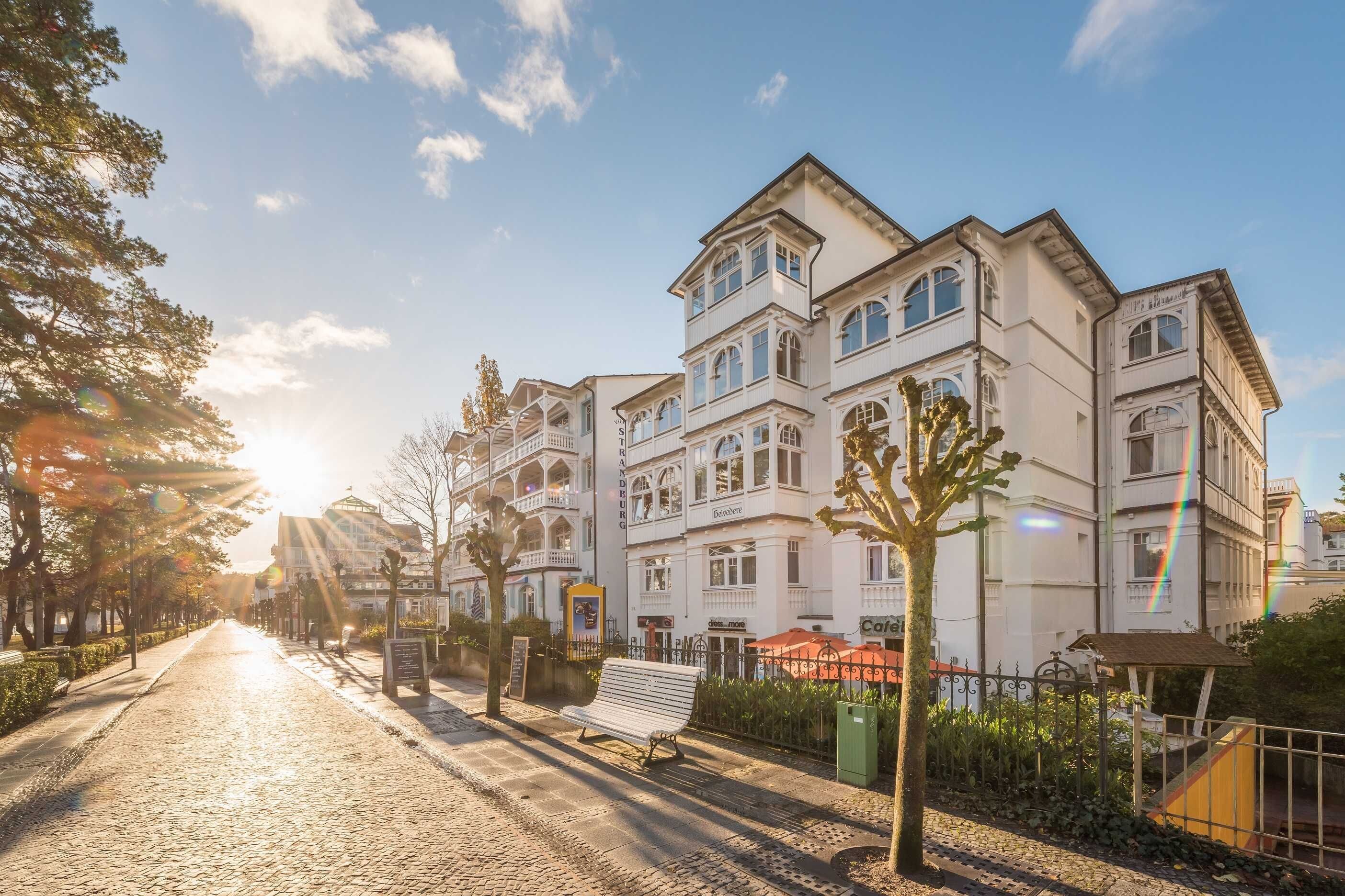 A multi-story building with a classic architectural style, a cobblestone street, and a bench along the sidewalk.