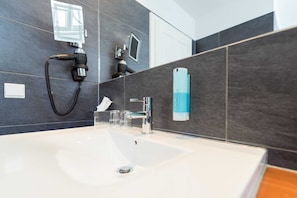 Une salle de bain moderne dotée d’un grand lavabo, d’une douchette à main, d’un miroir et d’un distributeur de serviettes.