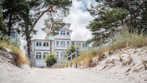 Un bâtiment situé sur la côte, doté d’une façade symétrique, d’un escalier menant à l’entrée et d’un chemin de sable.