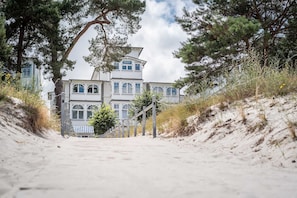 En byggnad belägen vid kusten med en symmetrisk fasad, en trappa som leder upp till entrén och en sandstig.