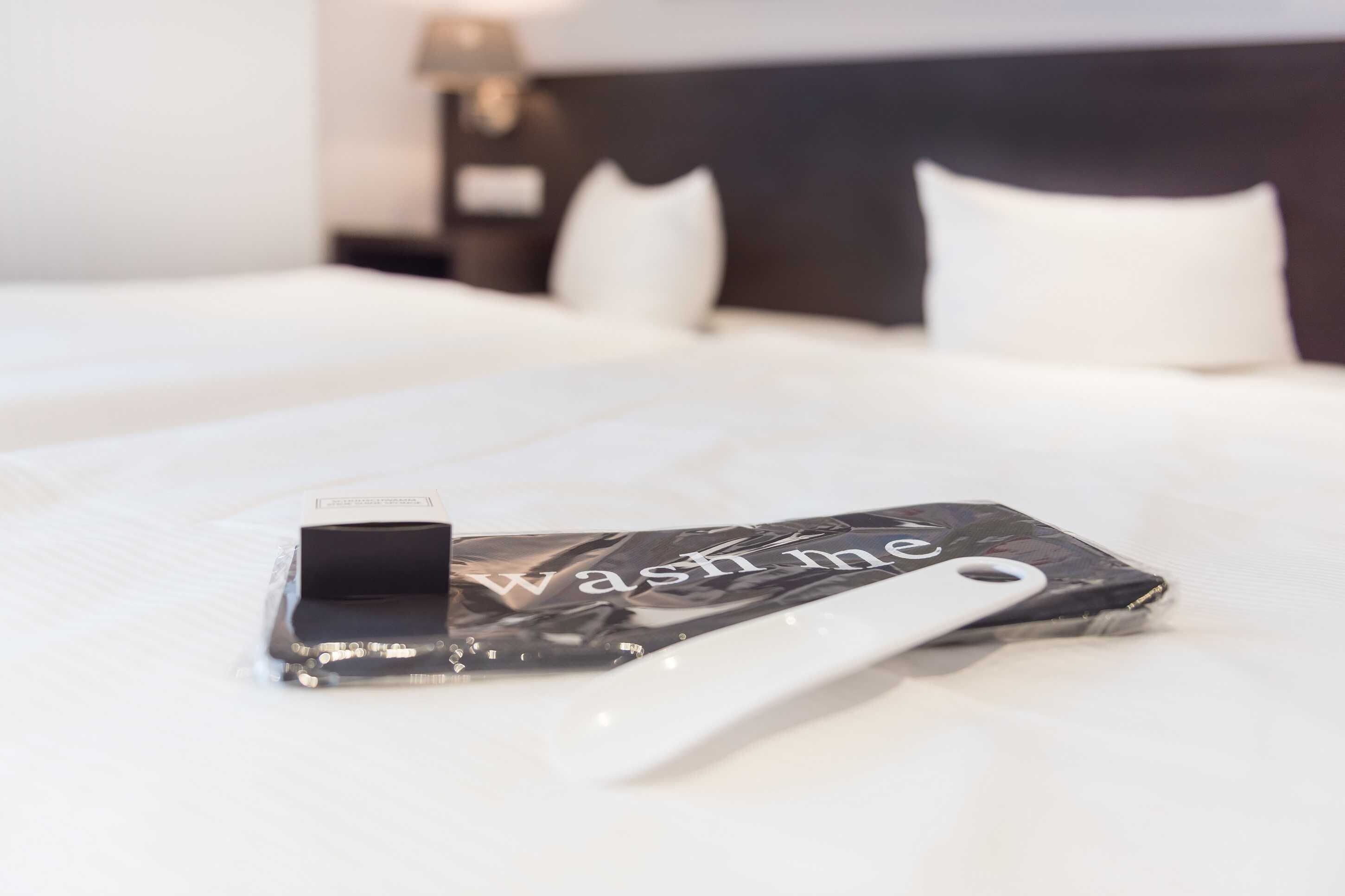 A neatly made bed with a white pillow and a black and white phone case with the text 'wash me' on it.