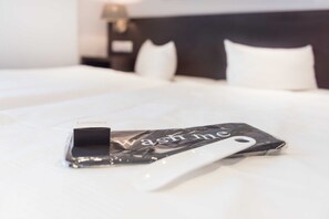 A neatly made bed with a white pillow and a black and white phone case with the text 'wash me' on it. - Double room with balcony - Hotel Villa Belvedere (Binz)