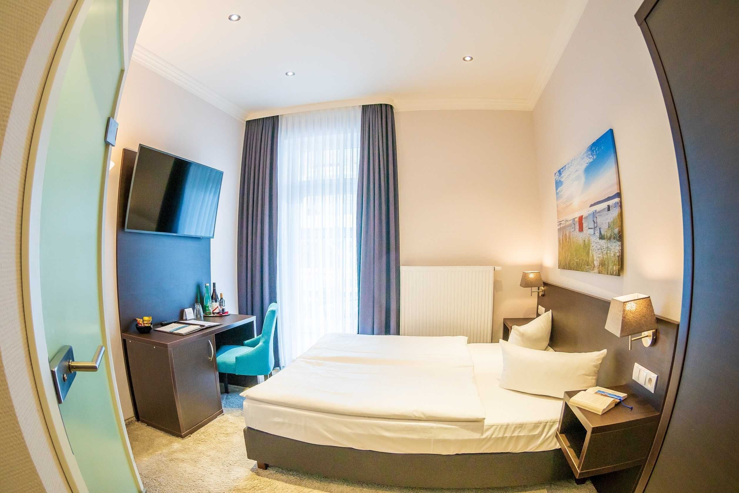 Een hotelkamer met een bed, een bureau, een stoel, een televisie en een schilderij aan de muur.