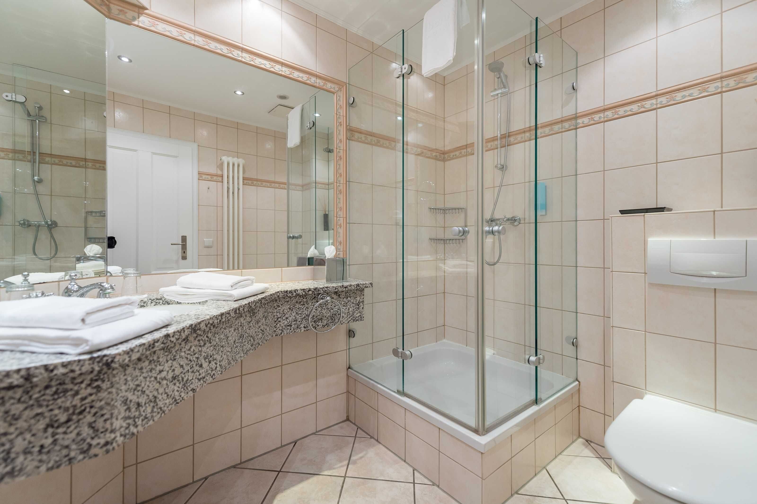 A modern bathroom with a glass-enclosed shower, a large mirror, and a granite countertop.