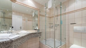 Un baño moderno con ducha envuelta en vidrio, un espejo grande y encimera de granito.