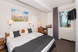 Une chambre d’hôtel équipée d’un lit, d’un bureau, d’une chaise, d’une télévision et d’une fenêtre donnant sur un paysage agréable.