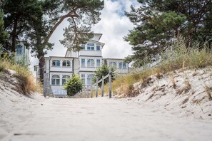 En byggnad belägen vid kusten med en symmetrisk fasad, en trappa som leder upp till entrén och en sandstig.
