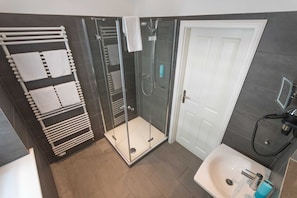 A modern bathroom with a glass-enclosed shower, a white sink, and a towel rack with multiple towels. - Junior suite with panoramic sea view - Hotel Villa Belvedere (Binz)