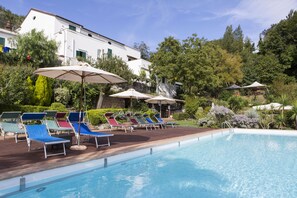 A poolside area with lounge chairs and umbrellas, surrounded by greenery and a building. - Villa Lupara (Salerno)