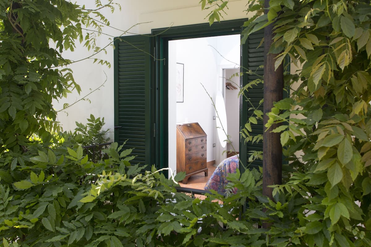 A room with a wooden dresser, a bed with a patterned bedspread, and a door leading to another room.