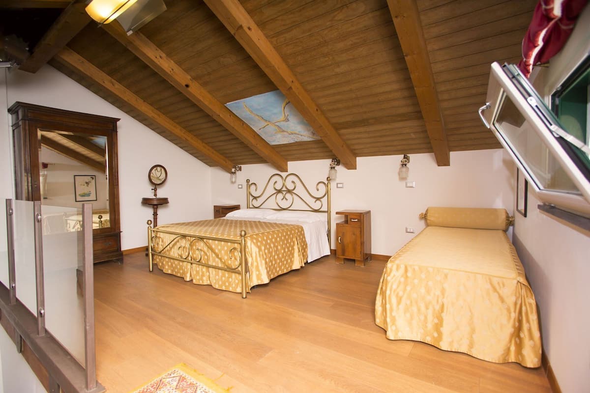A bedroom with two beds, wooden beams on the ceiling, a small window, and a mirror.