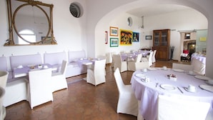 Un comedor con asientos tipo cabina blancos y mesas redondas, un espejo grande y obras de arte coloridas en las paredes.