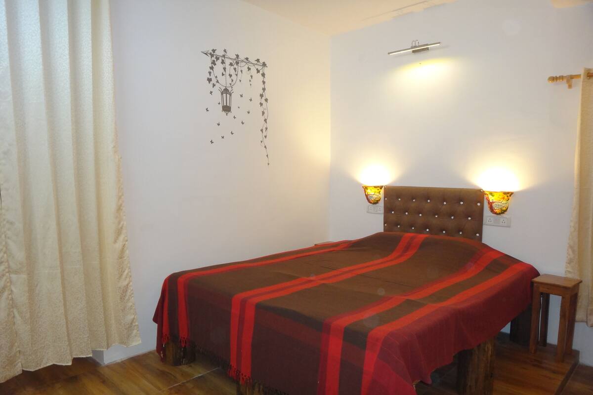 Een slaapkamer met een bed, houten vloer, witte muren en twee wandlampen.