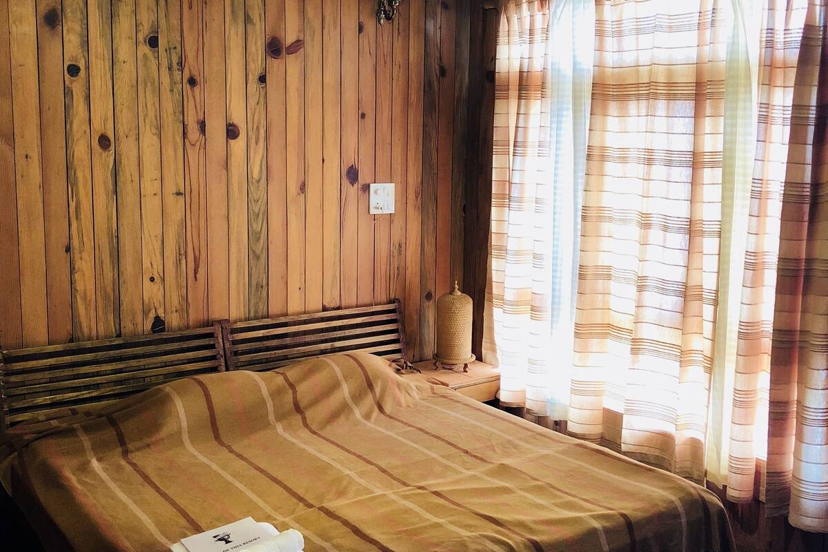 Een houten kamer met een bed, een hanglamp en gordijnen.