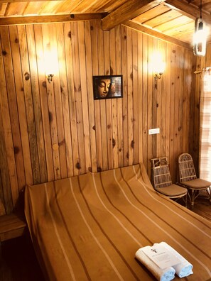 A wooden room with a bed, two wicker chairs, a wall-mounted picture, and a light fixture. - Aqua De Vida Resort (Nainital)