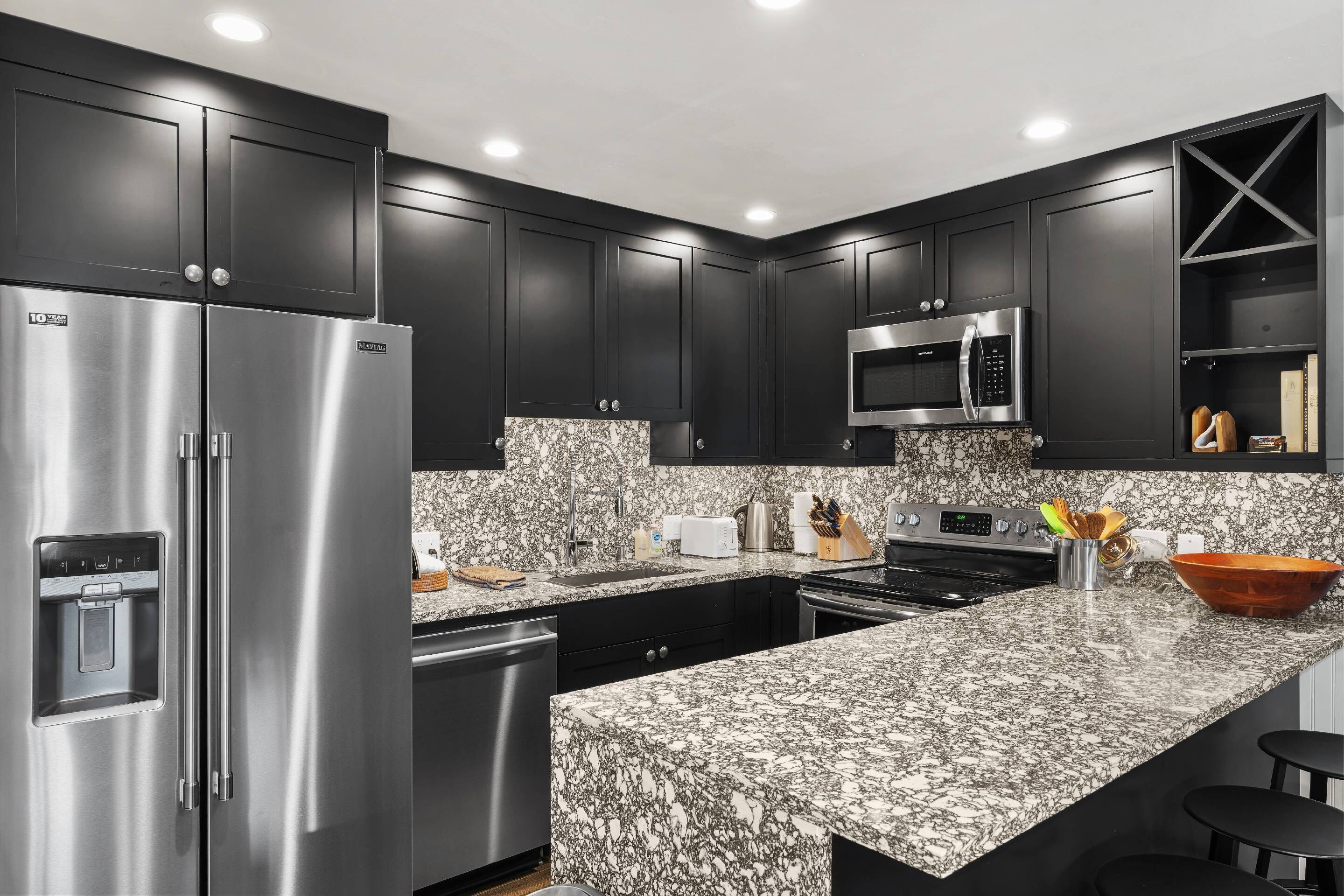 A modern kitchen with dark cabinetry, stainless steel appliances, and a granite countertop.