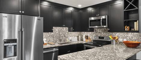 A modern kitchen with dark cabinetry, stainless steel appliances, and a granite countertop.