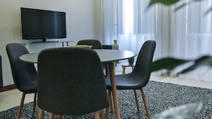 A modern dining area with a round table, four chairs, a flat-screen TV, and a vase on the table. - Casa do Teatro (Ponta Delgada)