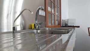A kitchen with a stainless steel sink, a faucet, and a microwave. - Casa do Teatro (Ponta Delgada)