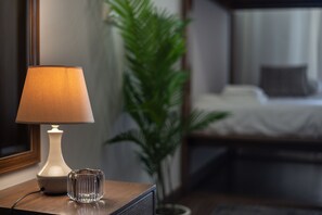 Une table de chevet avec une lampe et un vase en verre, une plante en pot, et un lit en arrière-plan.