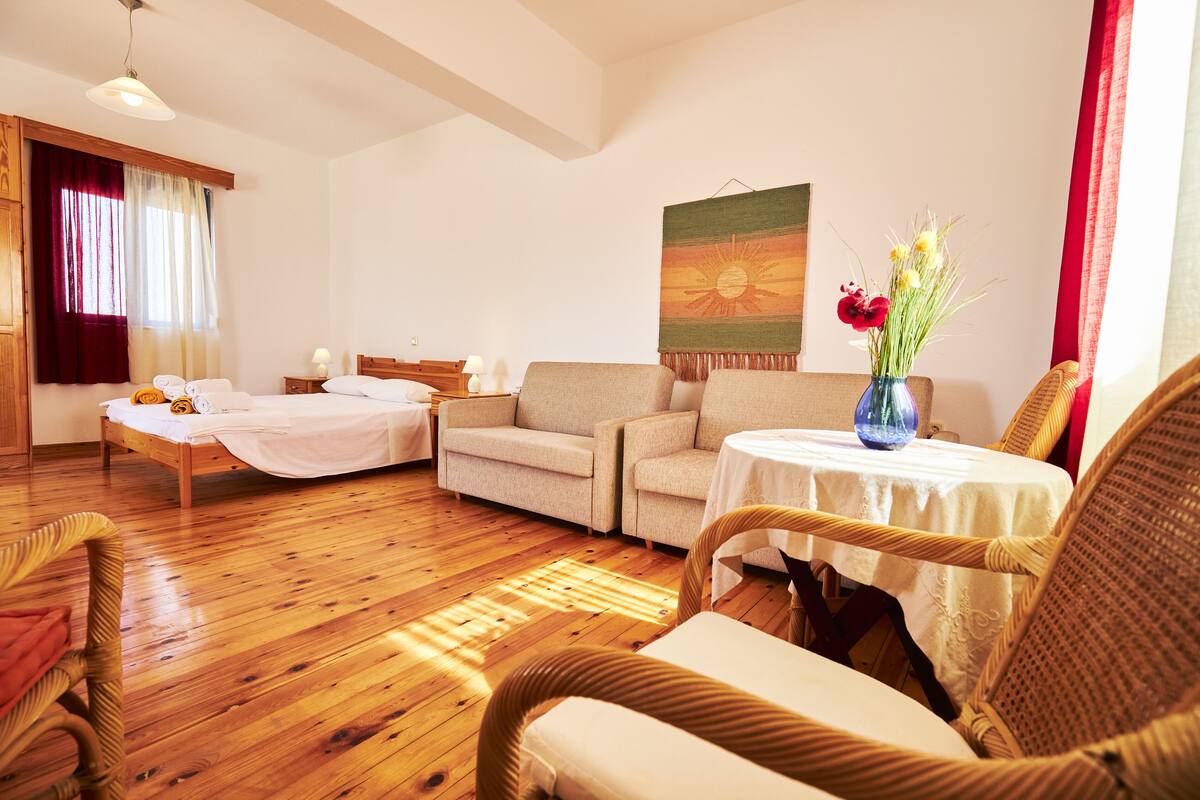 A cozy room with a bed, two sofas, a small table, and a wicker chair.