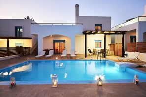 A swimming pool with lounge chairs and a covered seating area, surrounded by a modern building with a chimney. - Nerida Beachfront Villas (Rhodes)