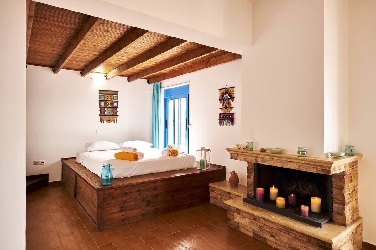 A bedroom with a wooden bed, a stone fireplace with candles, and a blue door.
