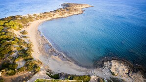 An aerial view of a coastal area with a sandy beach, rocky outcrops, and sparse vegetation. - Nerida Beachfront Villas (Rhodes)