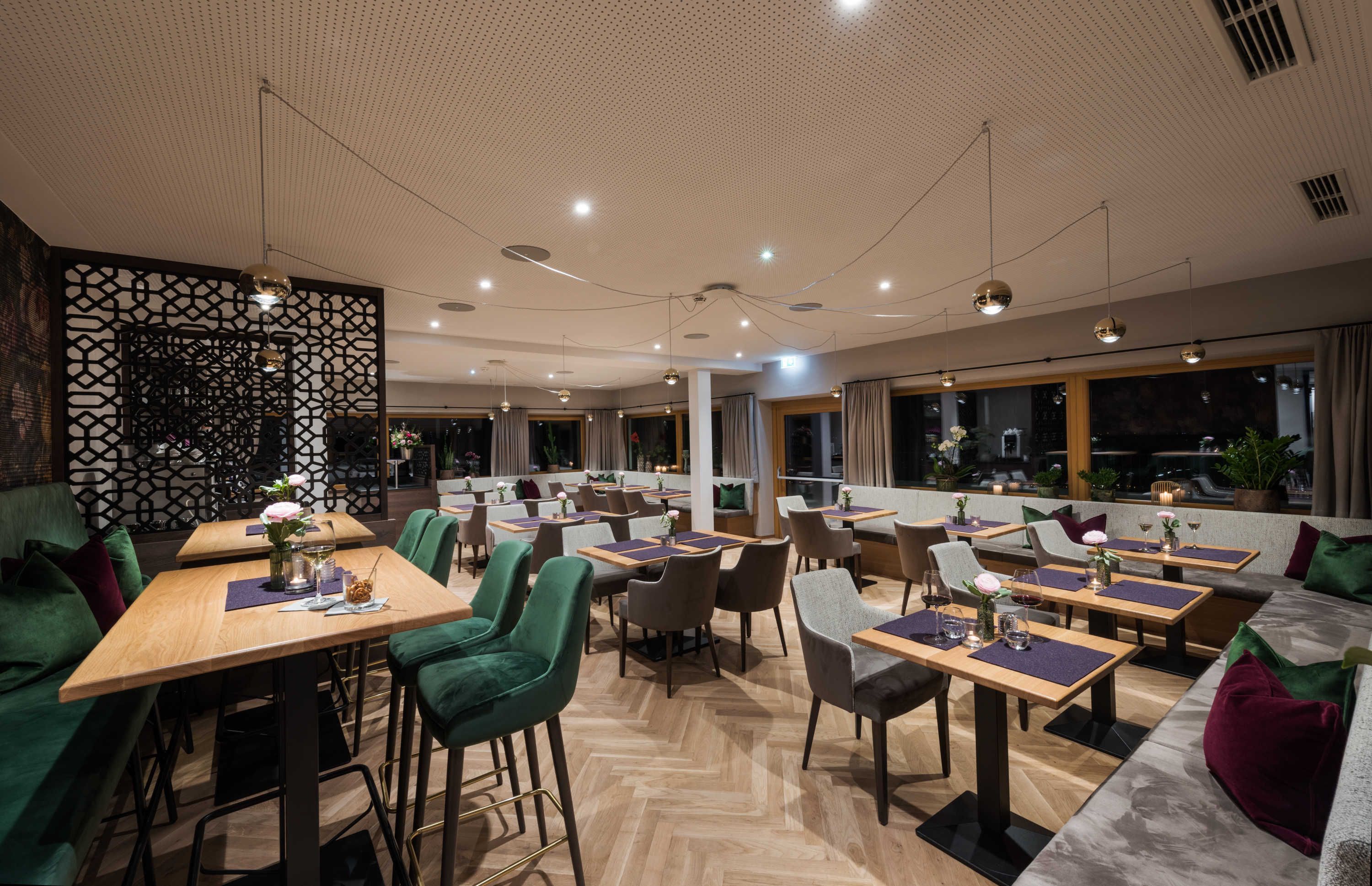 A modern restaurant with multiple dining areas, including booths and tables, with a decorative ceiling and large windows.