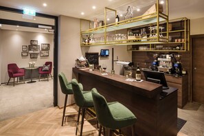 Un espace bar doté d’un comptoir en bois, de tabourets de bar verts et d’une étagère où sont rangés les verres.