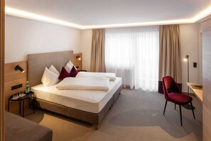 Een hotelkamer met een bed, een bureau, een stoel, een nachtkastje en een raam met gordijnen.