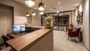Un comptoir d’accueil moderne, équipé d’un ordinateur, d’un vase de fleurs et d’un espace détente avec des fauteuils.