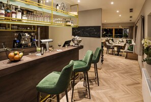 Una zona de bar con mostrador, taburetes y una variedad de botellas y vasos.