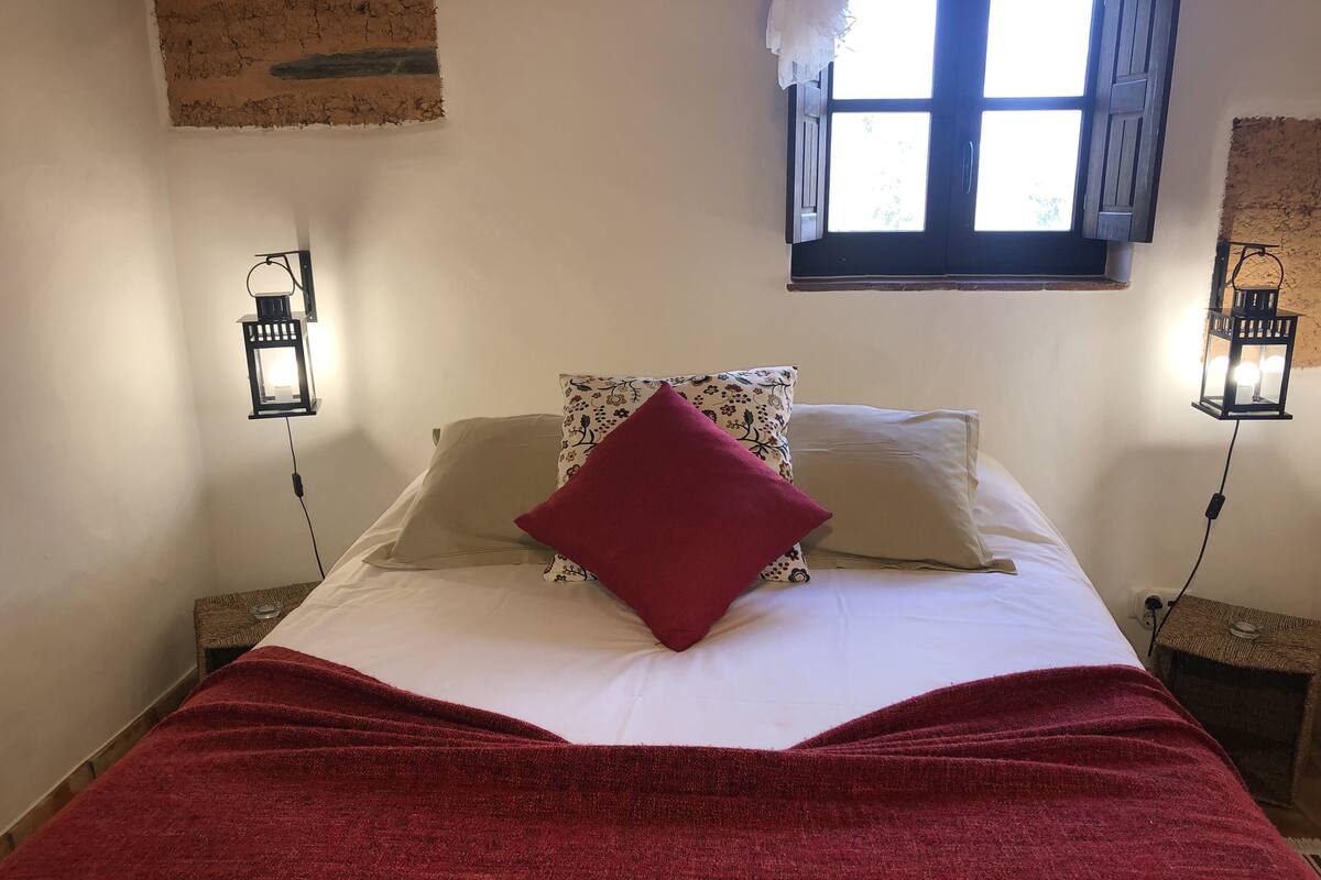 Ein Bett mit roter Decke, zwei Kissen und zwei Wandleuchten.