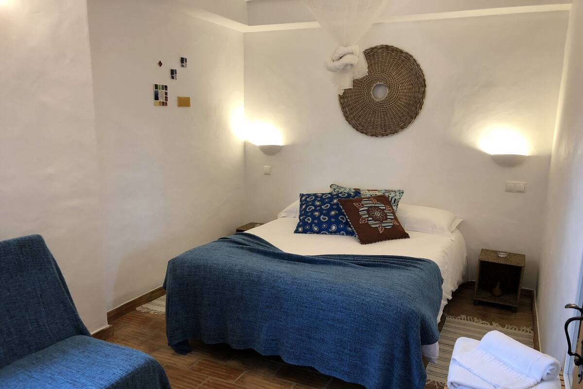 Ein Schlafzimmer mit einem Bett, einem Sessel, einem Nachttisch und einer Wandleuchte.