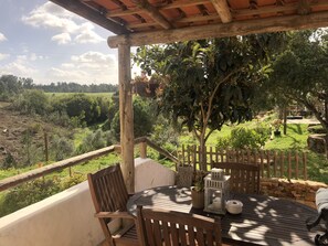 A wooden pergola with a table and chairs overlooking a lush garden and distant fields.