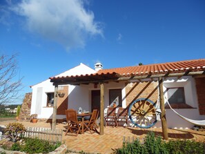 A white building with a red-tiled roof, a wooden pergola, and a large wheel. - Quinta das Beldroegas - Casas de Campo (Odemira)