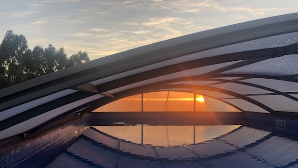 Une piscine dotée d’un toit en verre offrant une vue sur le coucher de soleil.