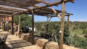 Une terrasse dallée de pierres, agrémentée d’une pergola en bois, de murs en pierre et offrant une vue sur un paysage verdoyant.