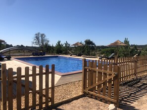 A swimming pool with a wooden fence, surrounded by pebbles and a clear blue sky. - Quinta das Beldroegas - Casas de Campo (Odemira)