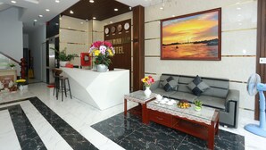 A hotel lobby with a reception desk, a sofa, a coffee table, and a painting of a sunset.
