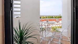 A balcony with a metal table and chairs, a potted plant, and a view of a cityscape.