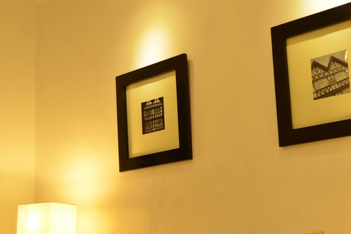 Una habitación de hotel con una cama, una mesita de noche con una lámpara y dos cuadros en la pared.