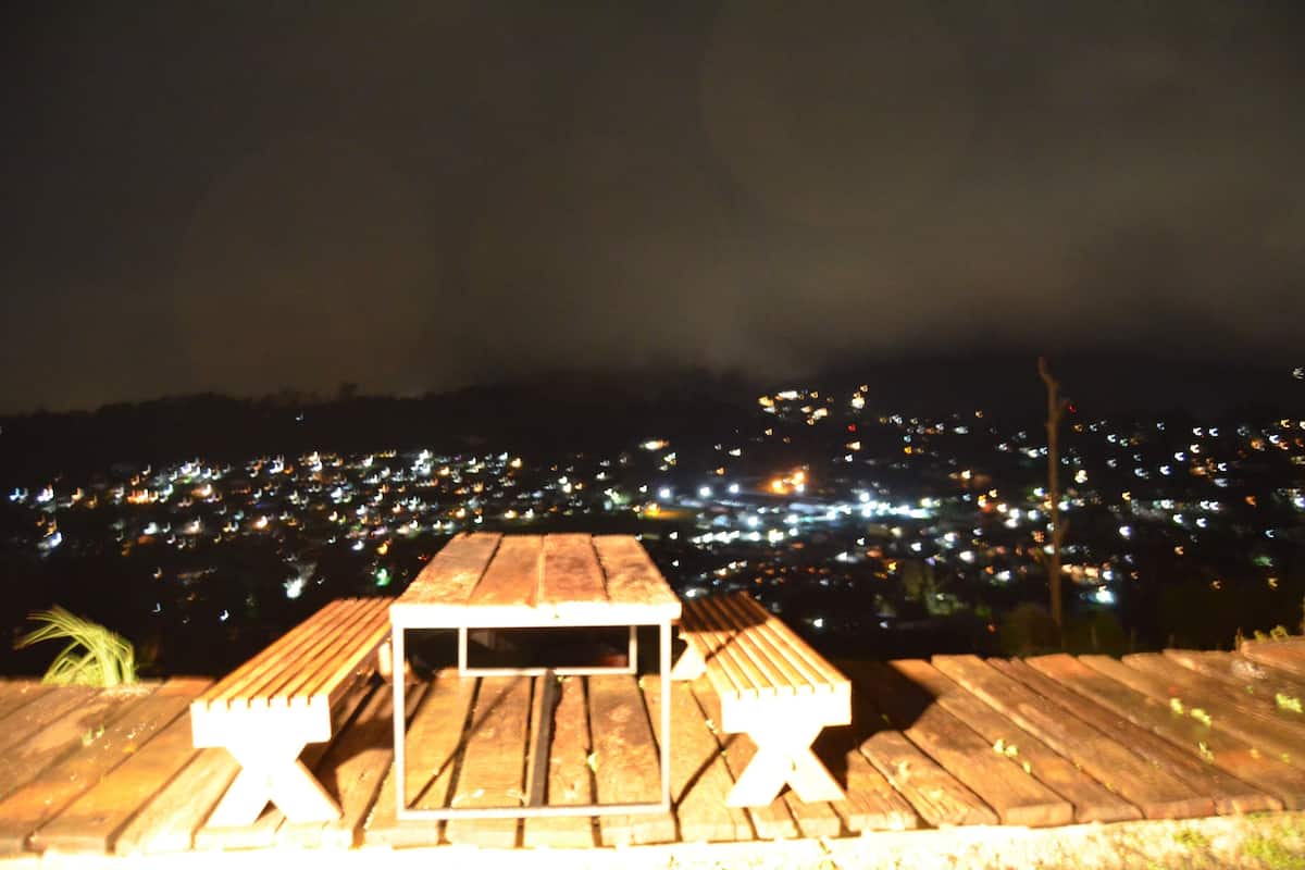 Terraza de madera con mesa y bancos, con vistas a un paisaje urbano nocturno.